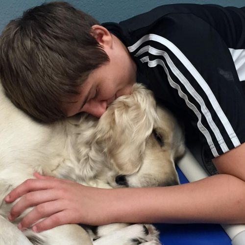 A student reading a book aloud to a facility dog